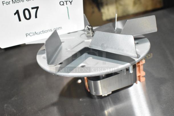 Brand new convection oven fan, metal construction, small scratches and dents, auction lot 107 tag visible.