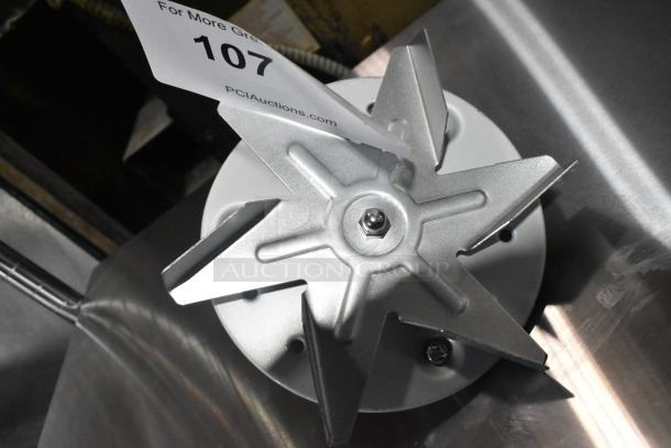 Brand new convection oven fan in metal, with minor scratches and dents. Auction tag reads "107" from PCI Auctions.