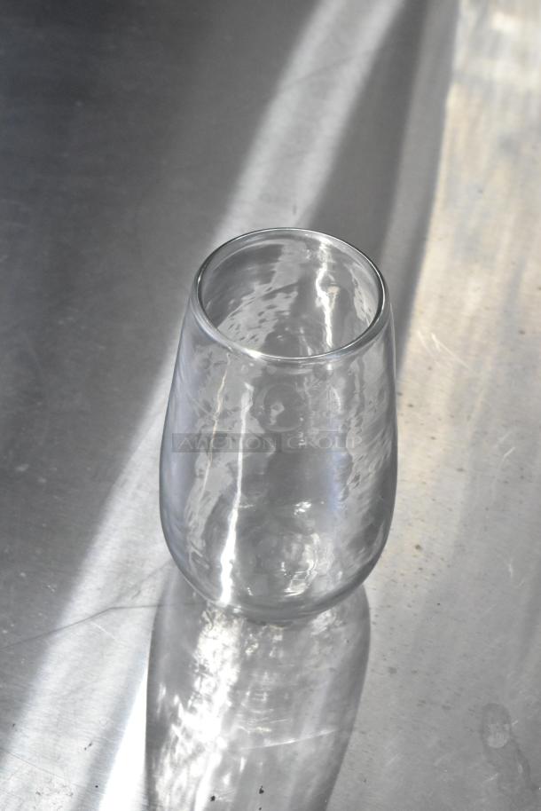 A clear glass tumbler with a subtle hammered texture displayed on a reflective surface.