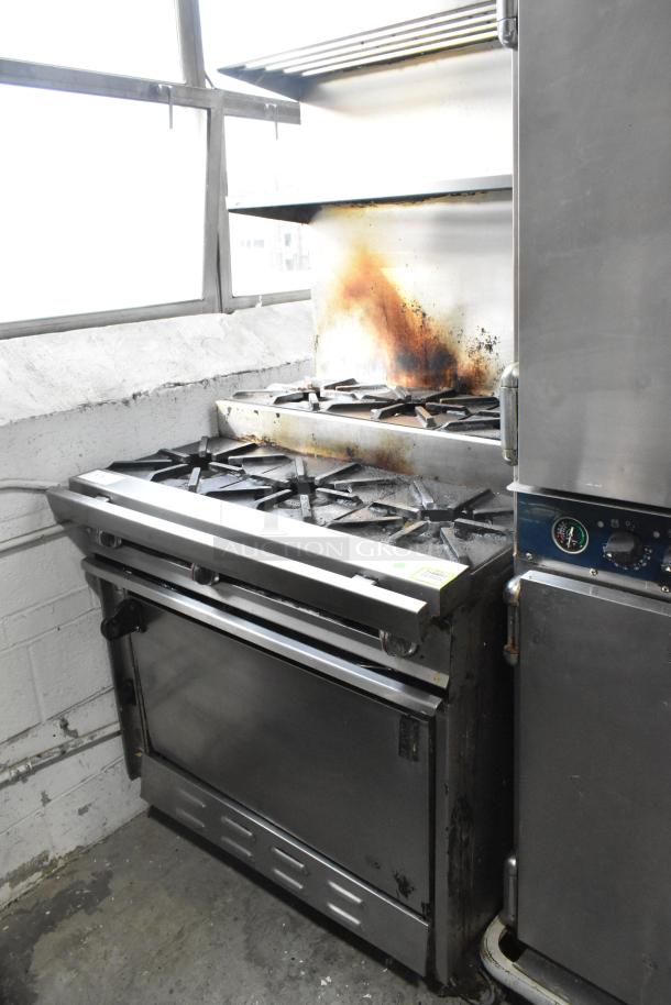 Montague stainless steel commercial flat top griddle with 2-tier, 6-burner range and oven. Equipped with back splash, commercial casters, 50,000 BTU, visible wear.