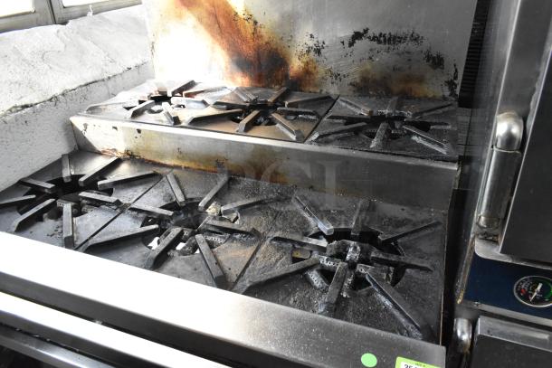 Montague stainless steel commercial gas griddle with 6 burner range and oven. Visible wear on backsplash. Equipped with casters.