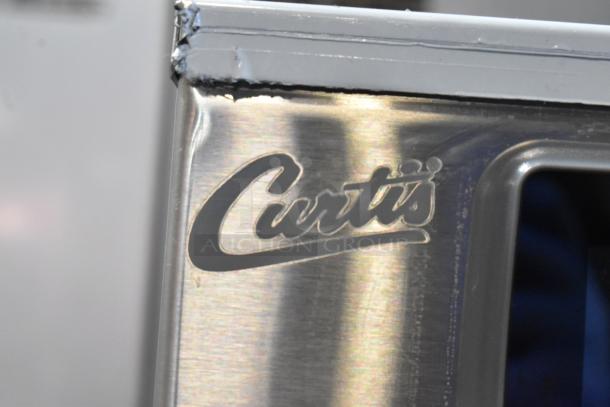 Curtis G4TBP stainless steel tea brewer close-up, featuring brand logo. Scratch and dent condition, 120V, 1-phase model.