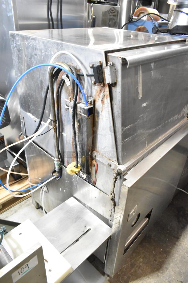 Stainless steel commercial undercounter glass washer, displaying surface wear and rust on connections, suitable for heavy-duty use.