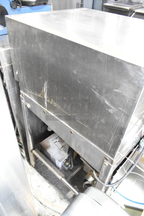 Stainless steel commercial undercounter glass washer, visible wear, sturdy construction, piping and wiring exposed, no labels visible.