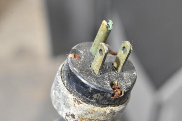 Close-up of a worn, rusted power plug from a Berkel E-222 meat grinder, showing signs of corrosion and wear.
