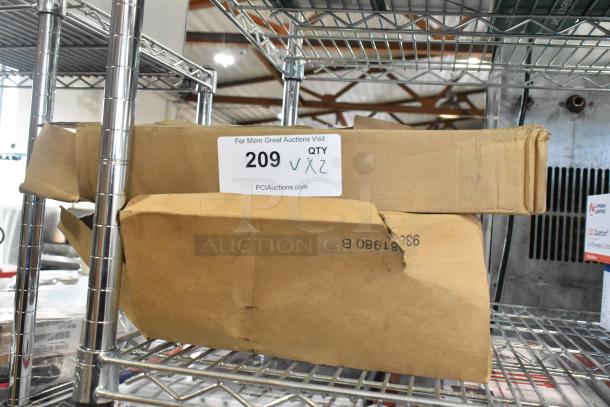 Cardboard boxes labeled "209" containing Dual-lite EVHC6IDP-WM LED wall light and Global 500874 LED exit sign. Boxes are dented but items are new.