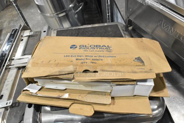Cardboard box labeled "Global Industrial" containing a LED Exit Sign Model No. 500874, showing minor wear.