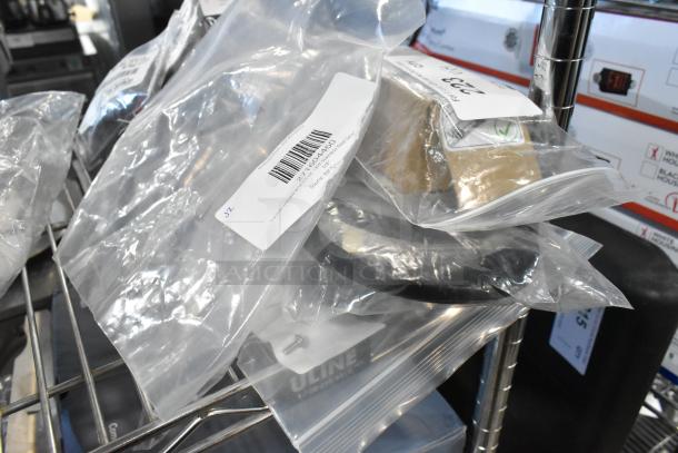 Four brand new items in sealed bags, including Carlisle stainless steel serving spoon and Estella upper belt. Tags show model numbers.