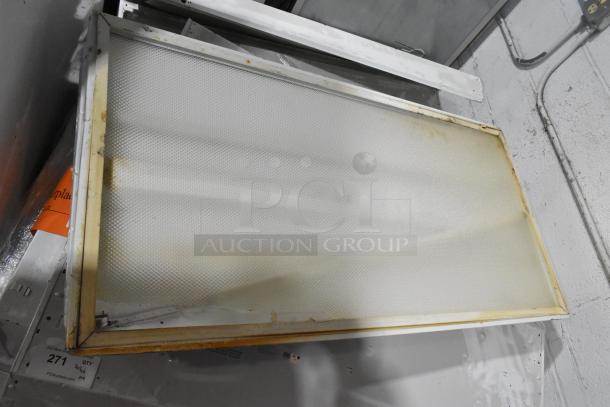 Pallet of fluorescent lights with white diffusers, showing signs of wear and discoloration. Auction lot tag visible.