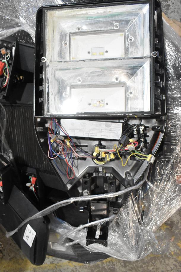 Assorted light fixtures with exposed wiring, wrapped in plastic. Includes labels indicating LED configuration and model numbers.