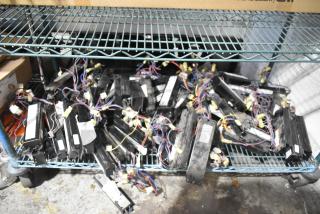 Lot of various electrical ballasts on a metal shelf. Items have wires and connectors, appear used, quantity unspecified.