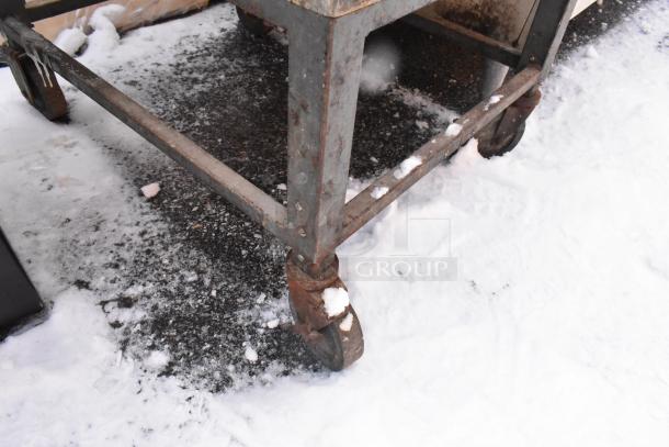 Hobart scale stand on commercial casters, metal frame, some rust, set on snowy pavement.