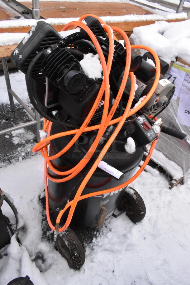 Husky C301H Air Compressor with orange hose, visible wear and snow, on wheels for portability.