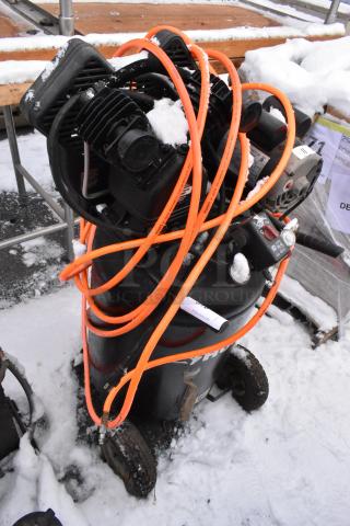 Husky C301H Air Compressor with orange hose, visible wear and snow, on wheels for portability.