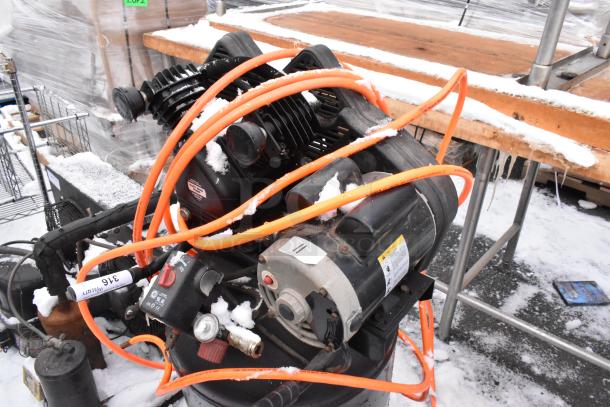 Husky C301H air compressor with visible hoses and wear, partially covered in snow. Model and safety label present.
