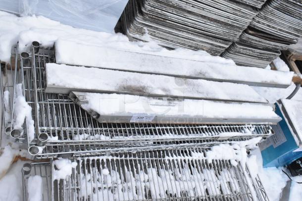 Pallet lot of various metal wire shelves covered in snow, showing moderate wear. Auction tag number 320 visible.