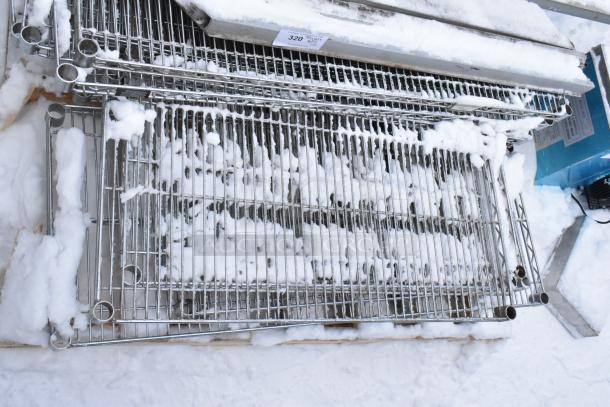 Pallet lot of various metal wire shelves covered in snow, showing multiple shelves with circular tube connectors.