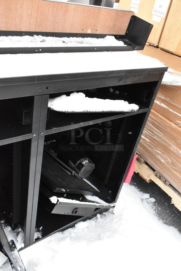 Two black metal counters, partially covered in snow. Features include open shelving and a wooden backing. Some wear visible.