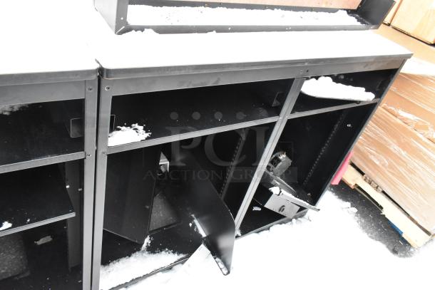 Two black metal counters with integrated shelves, lightly snow-dusted. Sturdy and functional, suitable for retail use.
