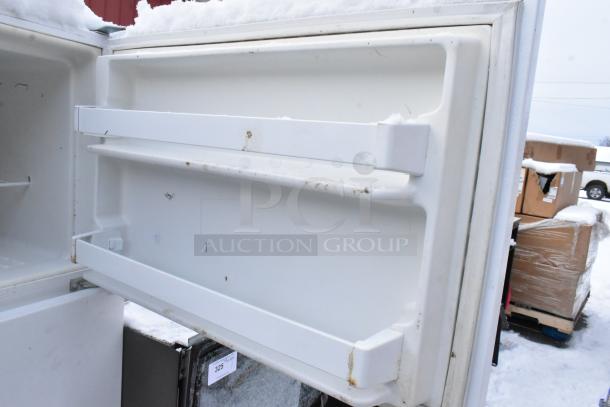 Maytag M1TXEGMYW01 reach-in cooler with freezer, open door showing interior shelves. Condition suggests outdoor storage.