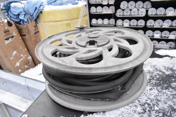 Round grey wheel with coiled black hose, outdoor setting with price tags in background, winter conditions visible.