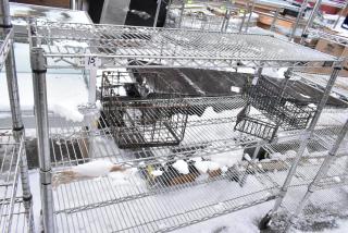 Chrome finish 3-tier wire shelf on commercial casters, outdoor setting, some snow accumulation, with attached storage baskets.