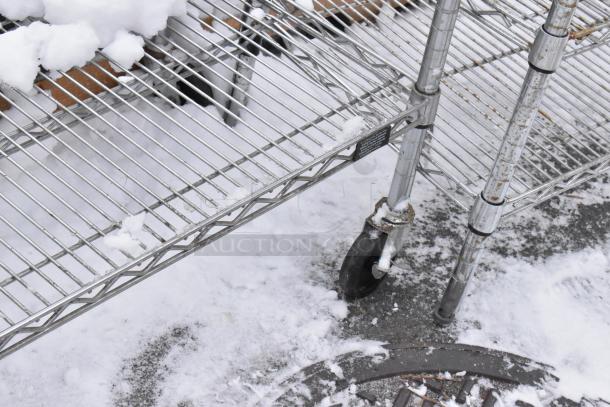 Chrome finish 3-tier wire shelf on commercial casters, snow-covered, needs dismantling for shipping. Ideal for heavy-duty storage.