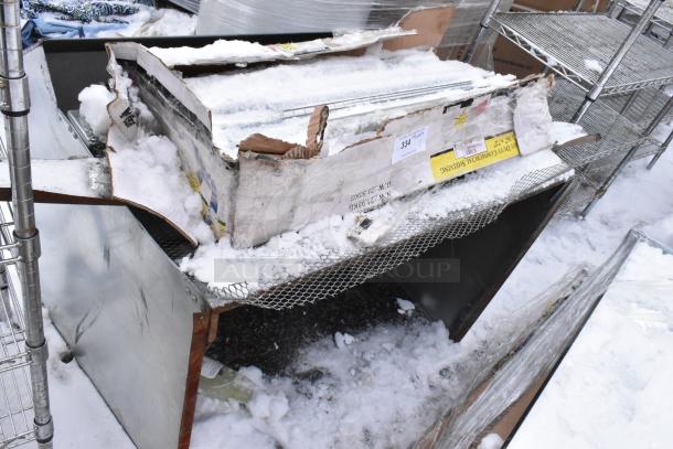 Heavy-duty commercial shelving unit in damaged box, covered in snow. Metal construction with some visible labels and markings.