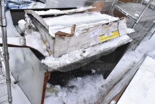 Heavy-duty commercial shelving unit in damaged box, covered in snow. Metal construction with some visible labels and markings.