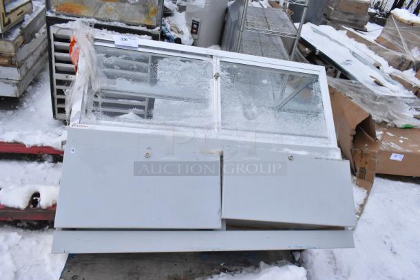 Gray metal display case merchandiser with glass sliding doors, shows signs of wear and snow. Features secure lock mechanism.