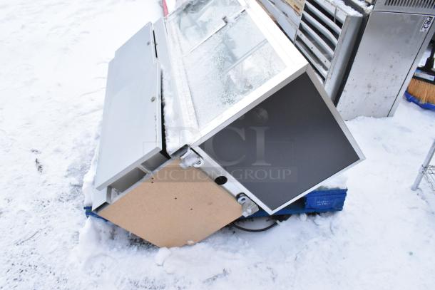 Gray Metal Display Case Merchandiser, snow-covered, with hinged glass door and a wooden panel on the side. Used condition.