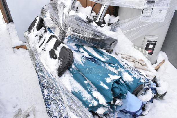 Pallet with Bradford White LD40S33B090 water heater and patio umbrellas, covered in snow, partially wrapped in plastic.
