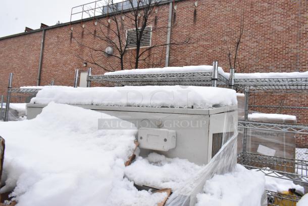 Snow-covered metal shelving units and HVAC unit in an outdoor yard, hinting at industrial use.