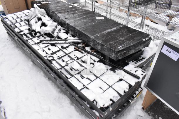Black poly shelving unit on a pallet with additional metal structures, covered partly in snow. Some markings visible.