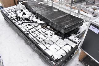 Black poly shelving unit on a pallet with additional metal structures, covered partly in snow. Some markings visible.