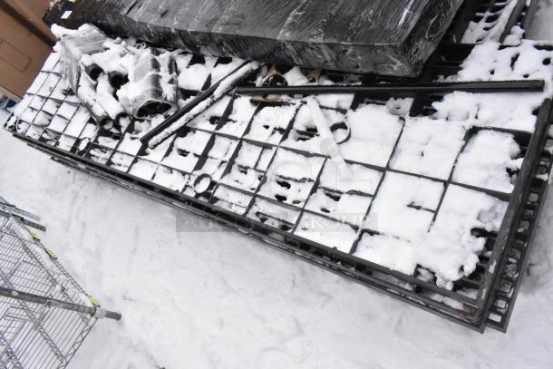 Pallet lot with black poly shelving unit, covered in snow. Includes multiple wrapped items and metal framework. Condition unclear.