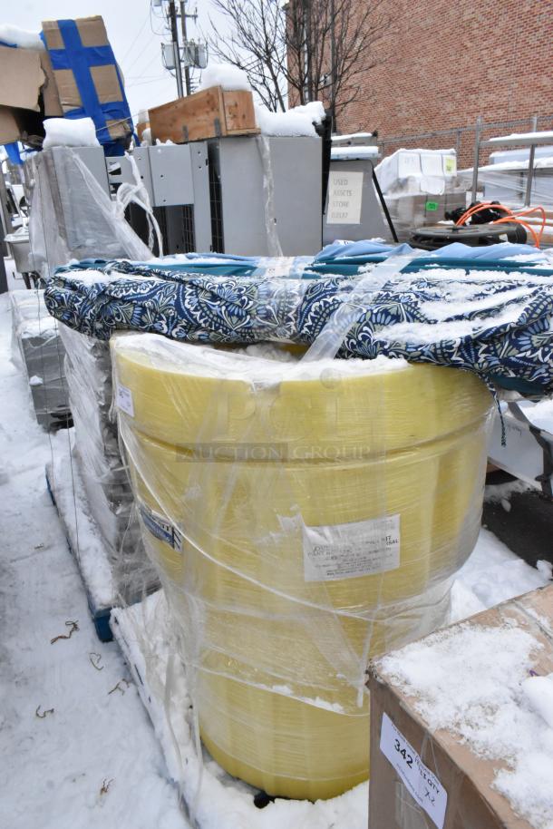 Yellow spill kit barrel with tags and blue patterned patio umbrellas, wrapped in plastic, on snowy outdoor pallet.