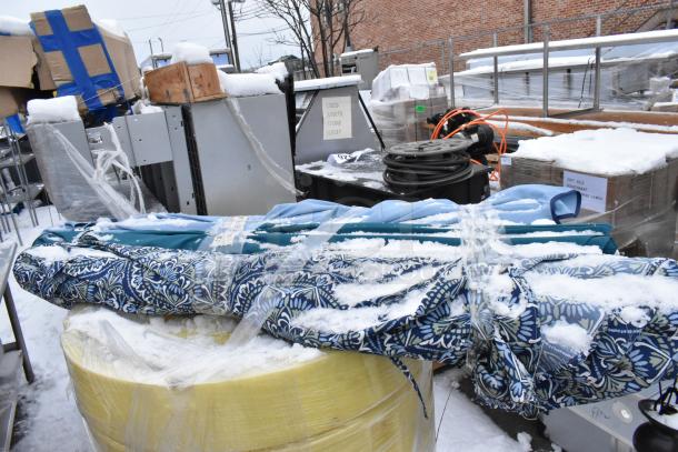 Four patio umbrellas with blue patterned fabric, snow-covered, atop yellow spill kit barrel. Auction lot includes additional items.