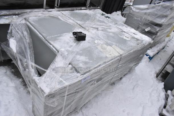 Large metal unit wrapped in plastic film, partially covered in snow. Includes a small black box on the surface. Appears in good condition.