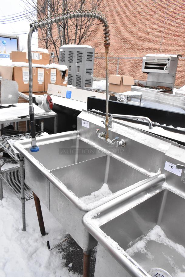 Stainless steel 2 bay sink with faucet, spray nozzle, and handles. Includes visible labels and integral backsplash. Snow-covered condition.