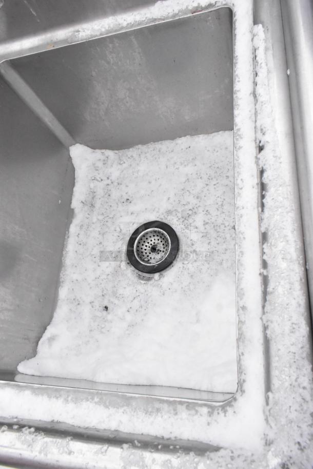 Stainless steel 2 bay sink with faucet and spray nozzle, showing one basin's inside surface. Used condition, cleanable grime.