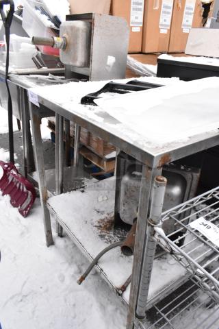 Metal work table with rusted edges, featuring an under shelf storing mixed contents, including hoses and boxes. Snow on surface.