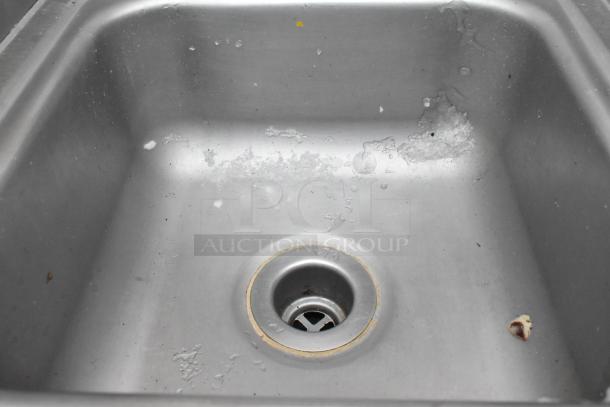 Stainless steel single bay wall mount sink with faucet, handles, side splash guards. Shows signs of wear.