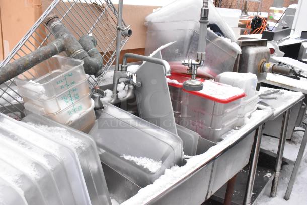 Stainless steel 3-bay sink with left side drain board, containing poly bins, surrounded by snow, used condition.