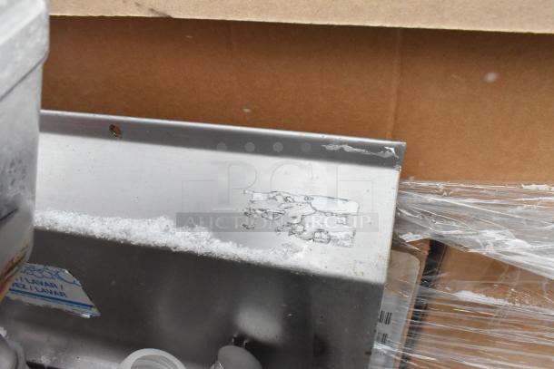 Stainless steel 3-bay sink with left side drain board, visible wear. Includes contents like poly bins. Features labels and markings.