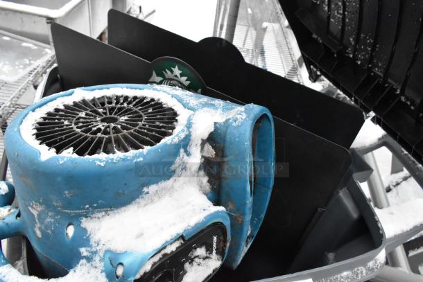 Blue fan inside a snow-covered poly trash can with various contents, indicating versatile use and storage.