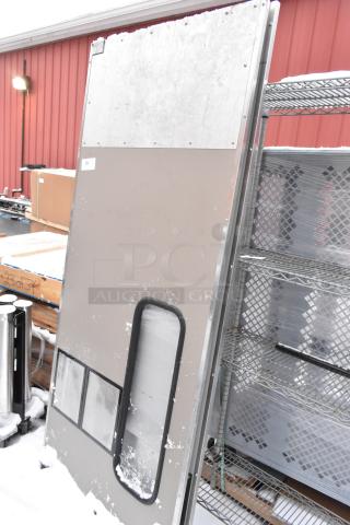 Two metal swinging kitchen doors in fair condition, snow-covered, with rectangular windows and visible metal frames.