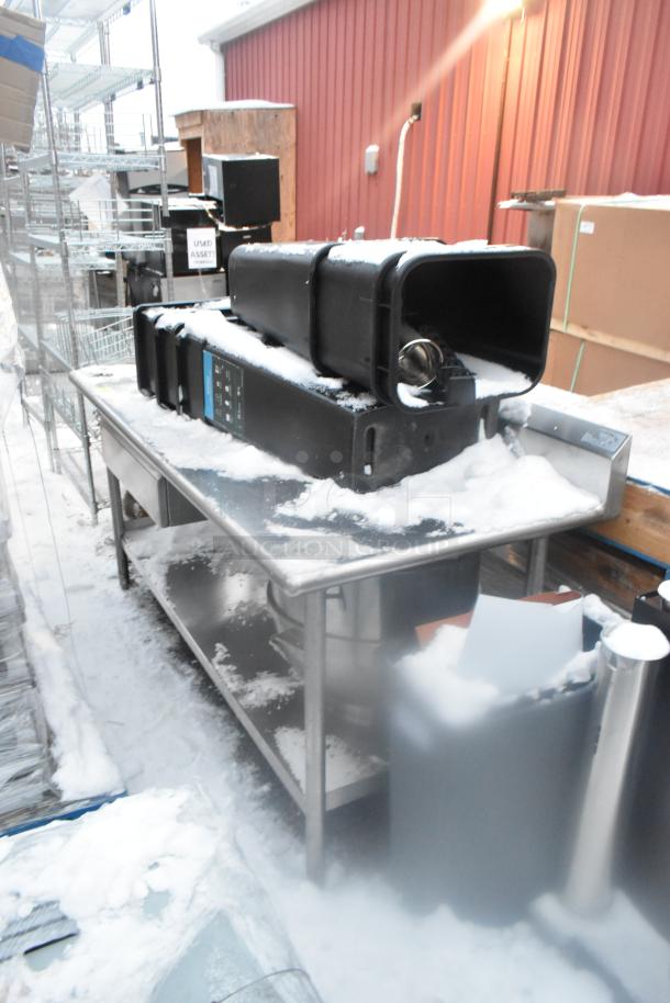 Stainless steel table with under shelf, snow-covered surface, includes poly trash cans. Outdoor setting. Used condition.