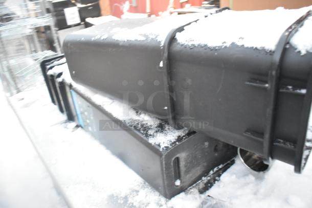 Stainless steel table with under shelf, snow-covered poly trash cans on top, visible wear, ideal for storage.