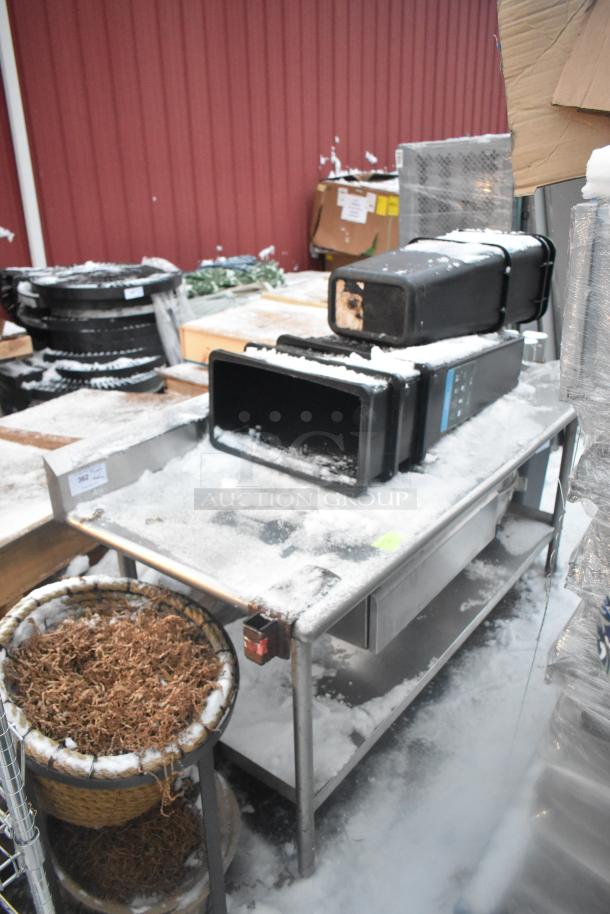 Stainless steel table with under shelf, holding poly trash cans, snow-covered. Signs of outdoor exposure.